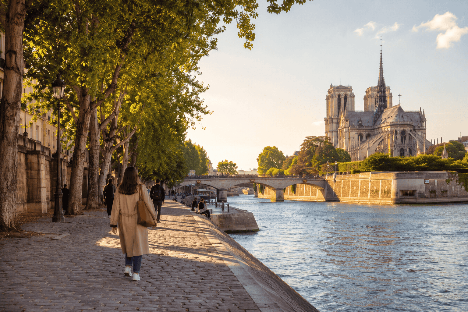 People walking along the Seine River in Paris at golden hour